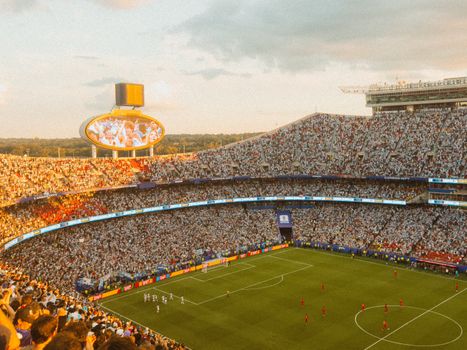 Aerial view of a packed soccer stadium during a lively match at sunset.